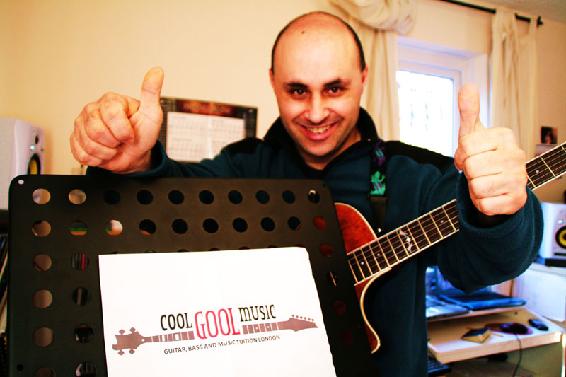 Malcolm Callus in his London studio, giving a thumbs-up beside a Cool Gool Music music stand with an archtop guitar on his shoulder