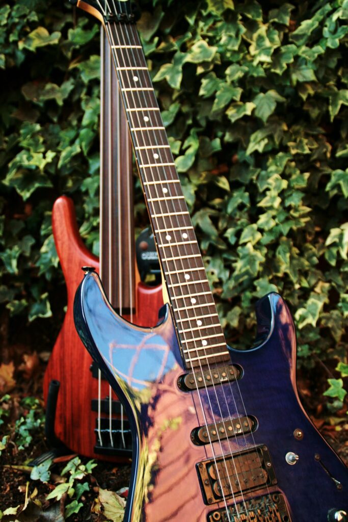 A blue electric guitar and a red bass guitar against a wall of ivy