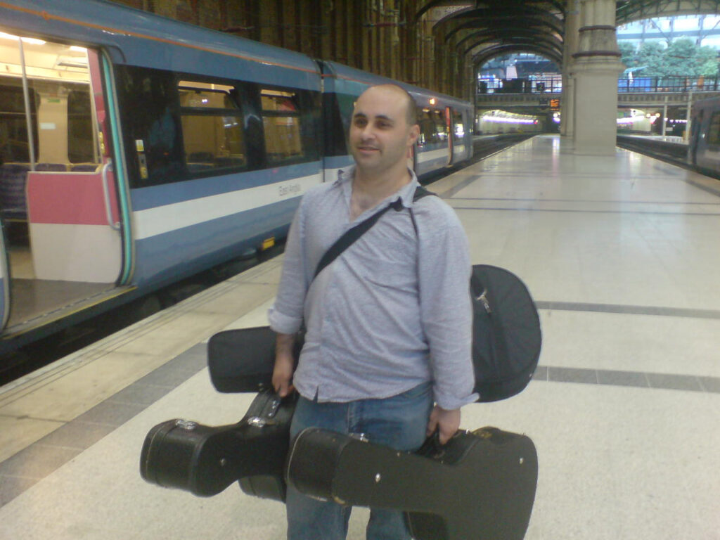 Malcolm Callus, guitar cases over each shoulder, on a station platform on his way to a home lesson